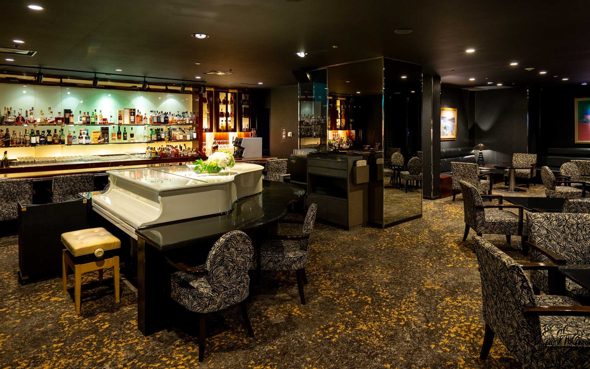 落ち着いた雰囲気のメインバー 夜間飛行内観　様々な銘酒、ボトルが並ぶバーカウンター　店内にはピアノも