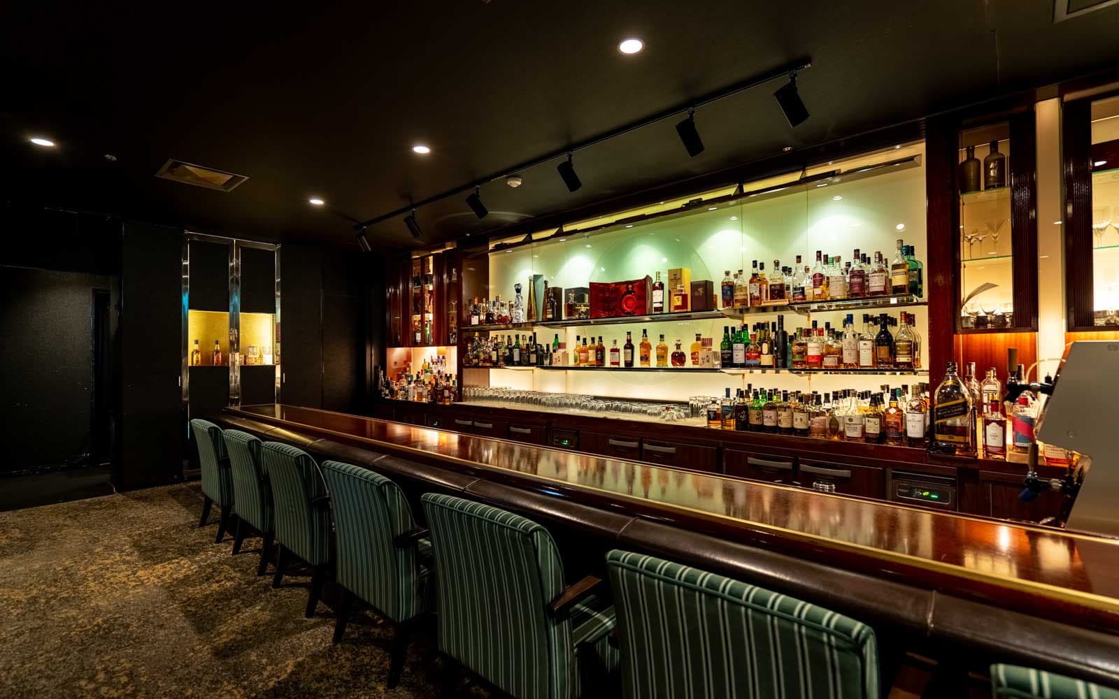 暖色系の照明に美しく照らされたリキュール棚とカウンター